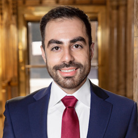 Professional portrait of Aaron Diaz in a blue suit with red tie. 