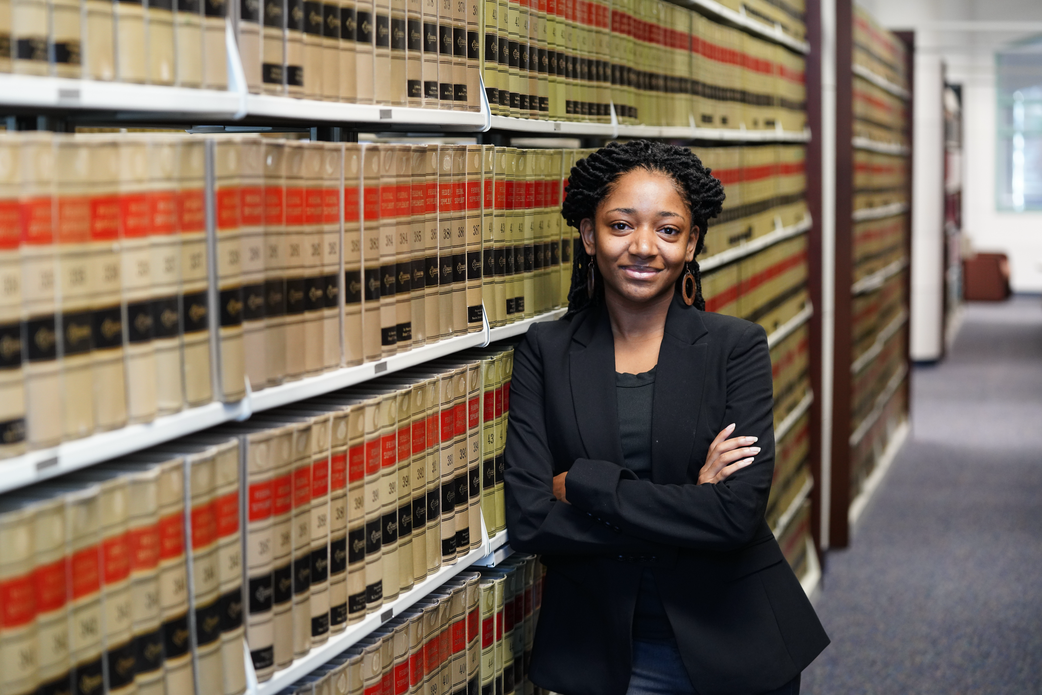 Female student wearing a suit leans against the bookcase in the law library.