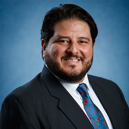 Professional portrait of Joaquin Gonzalez, Assistant Professor of Practice of Law, wearing a dark suit, white shirt and blue tie. 