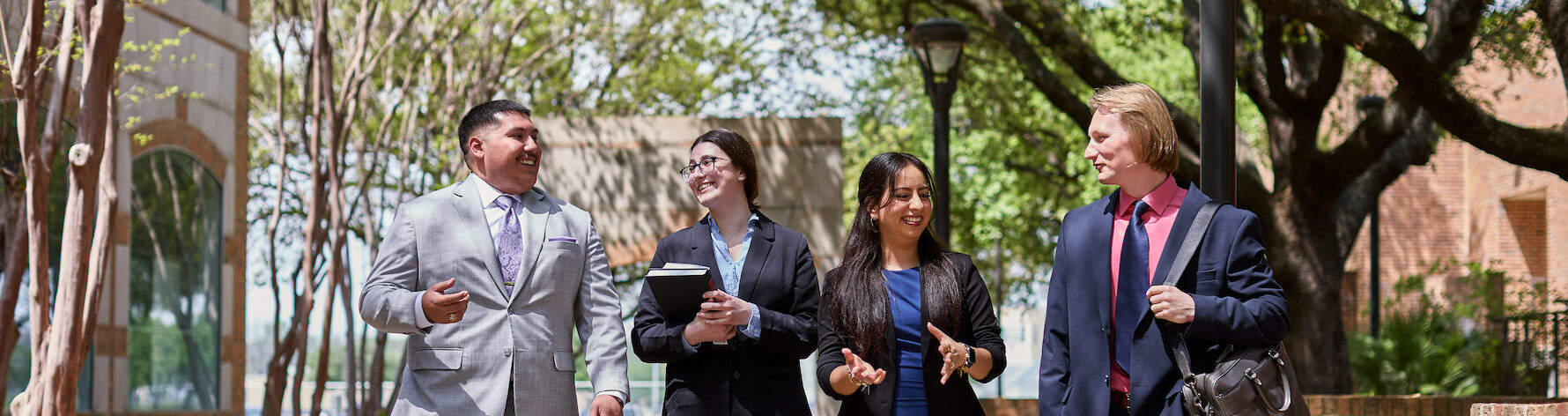 four students walk together holding books outside the school of law