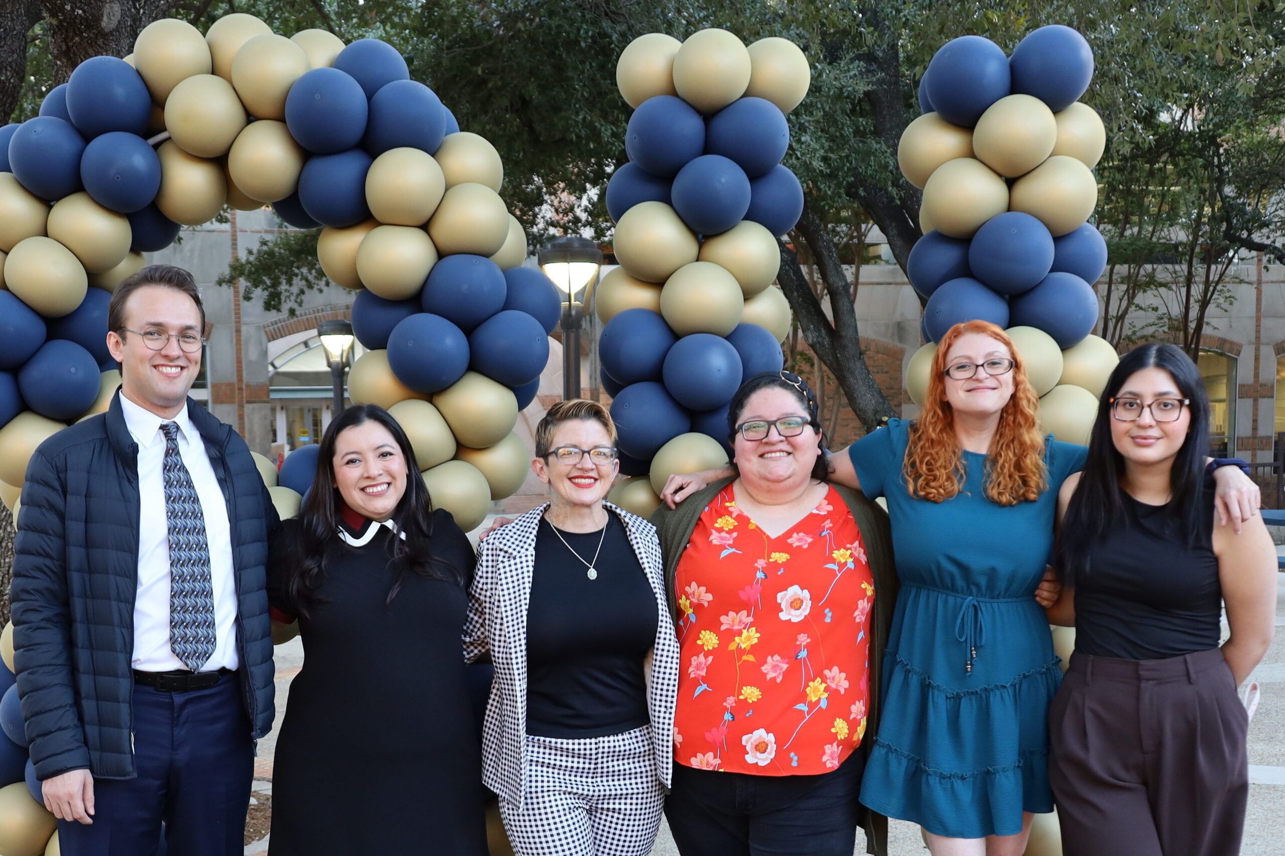 Group of people stand in front of a blue and gold balloon arch for a photo.